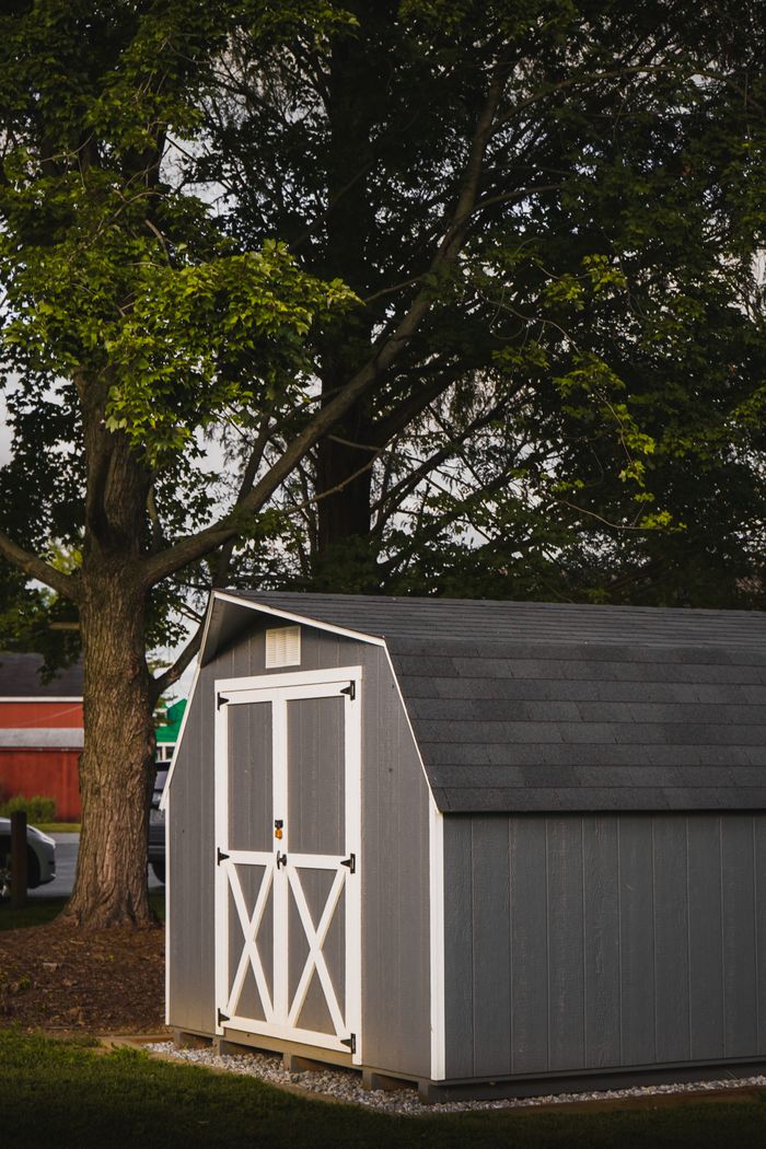A quaint gray garden shed nestled under lush trees in a serene backyard.