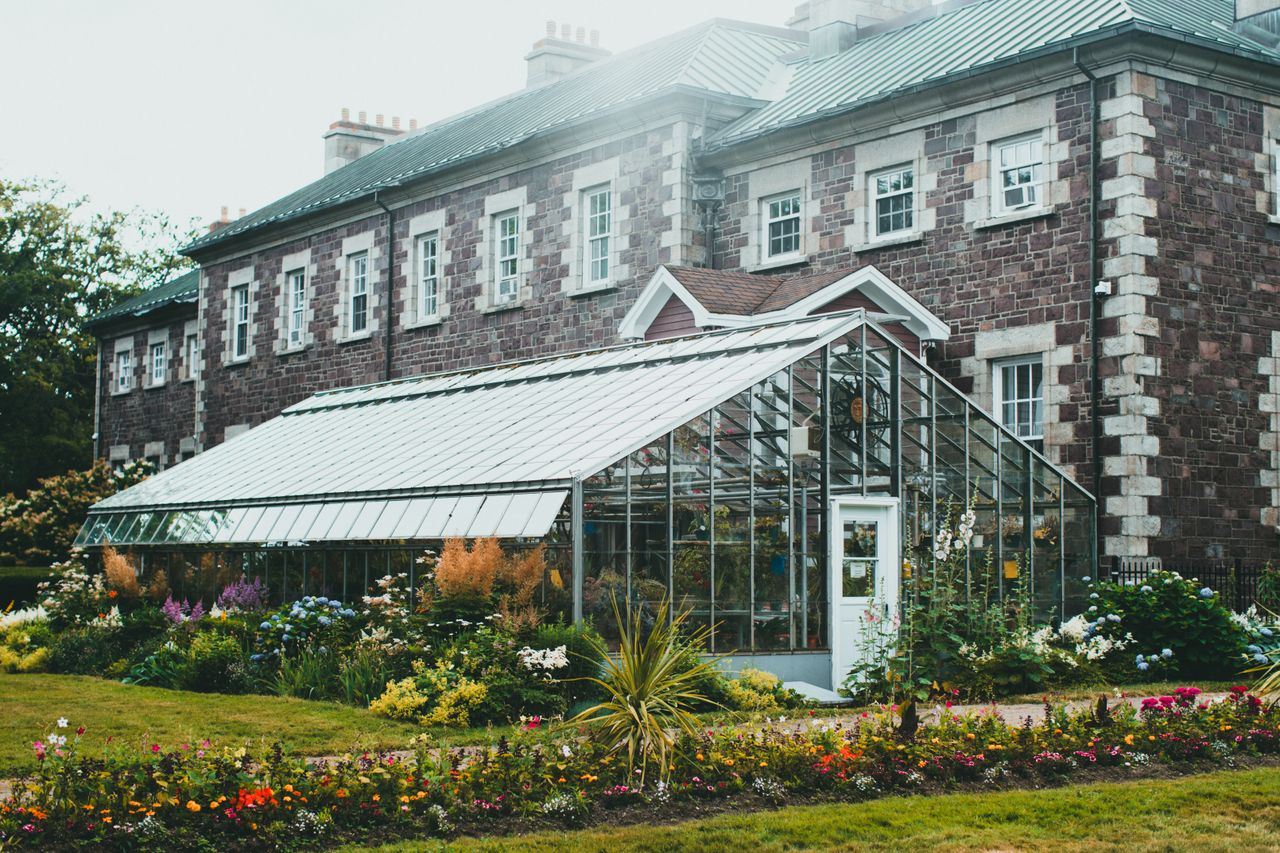 Mastering the First Impression: Your intriguing post title goes here A picturesque greenhouse surrounded by vibrant gardens against a historic stone building.