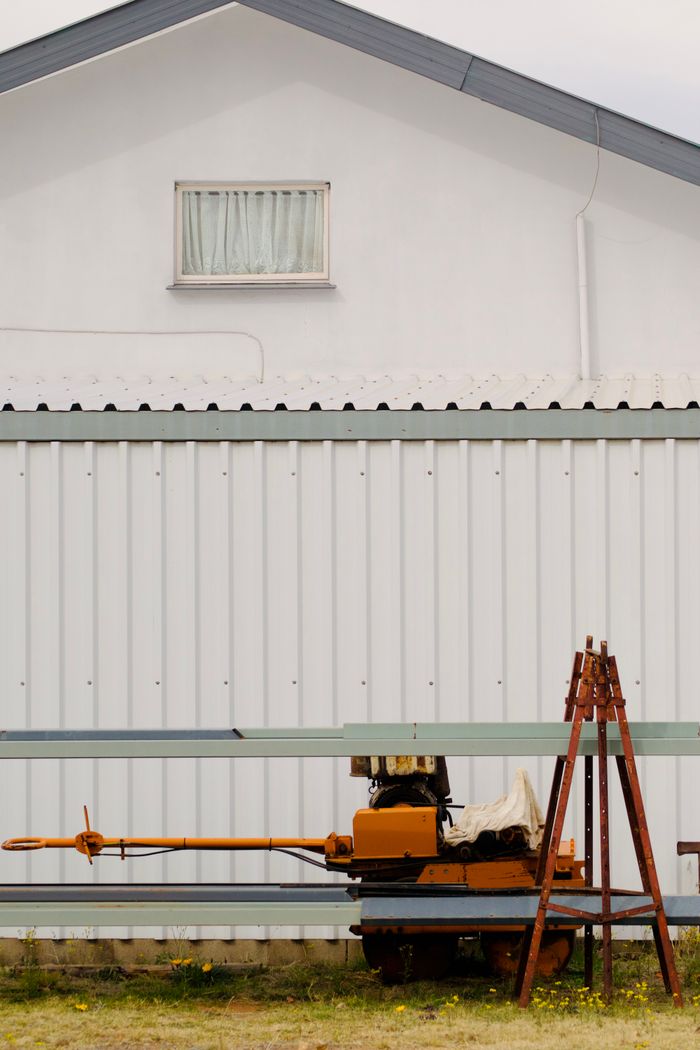 About Rusty industrial equipment by a white building exterior, showcasing storage or farm tool setting.